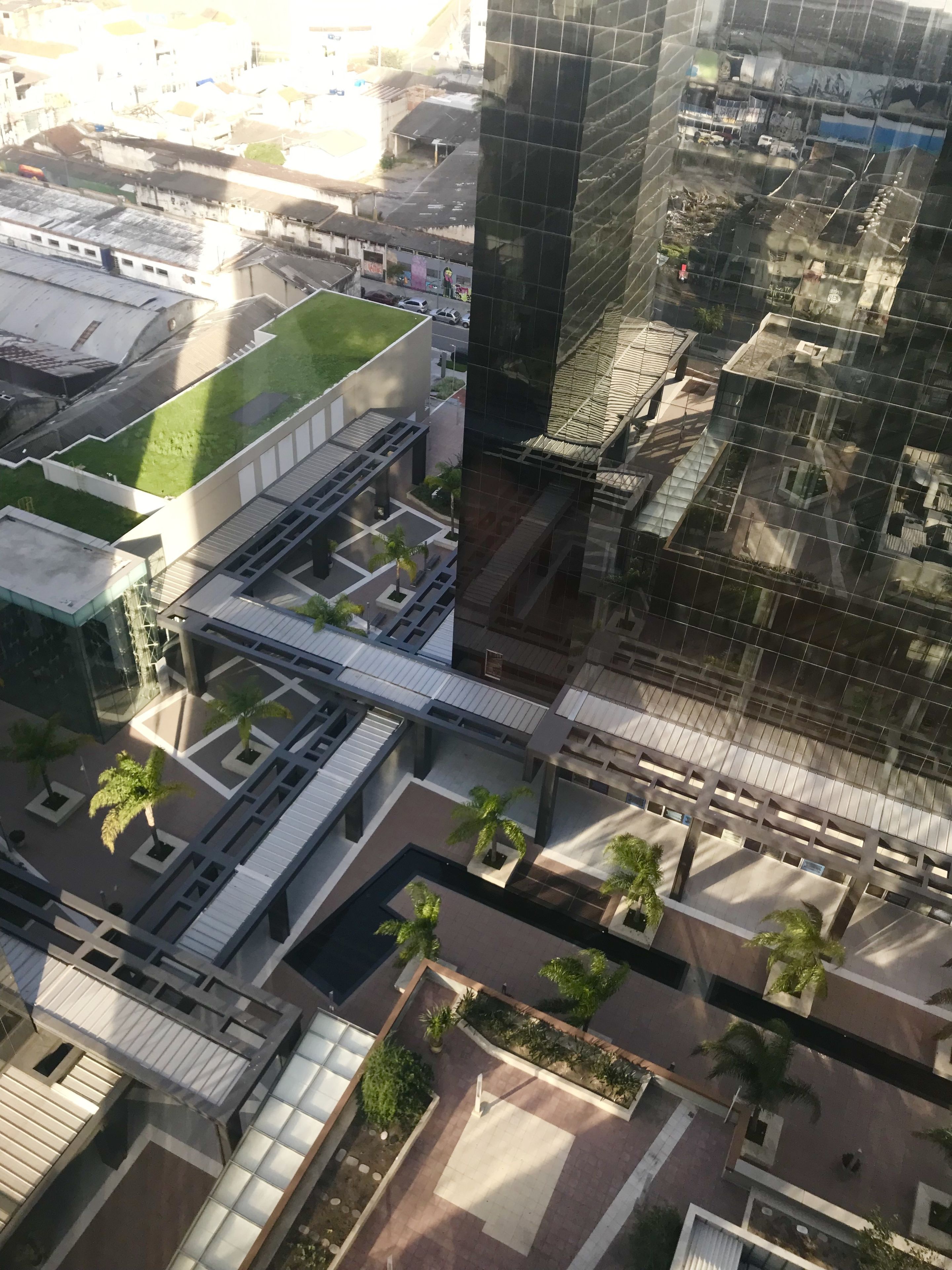 An aerial view of a modern building with a green roof, a covered pedestrian walkway, and surrounding urban landscape.