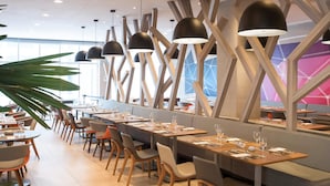 A modern restaurant with long communal tables, wooden chairs, and black pendant lights. - Novotel RJ Porto Atlântico (Rio de Janeiro)