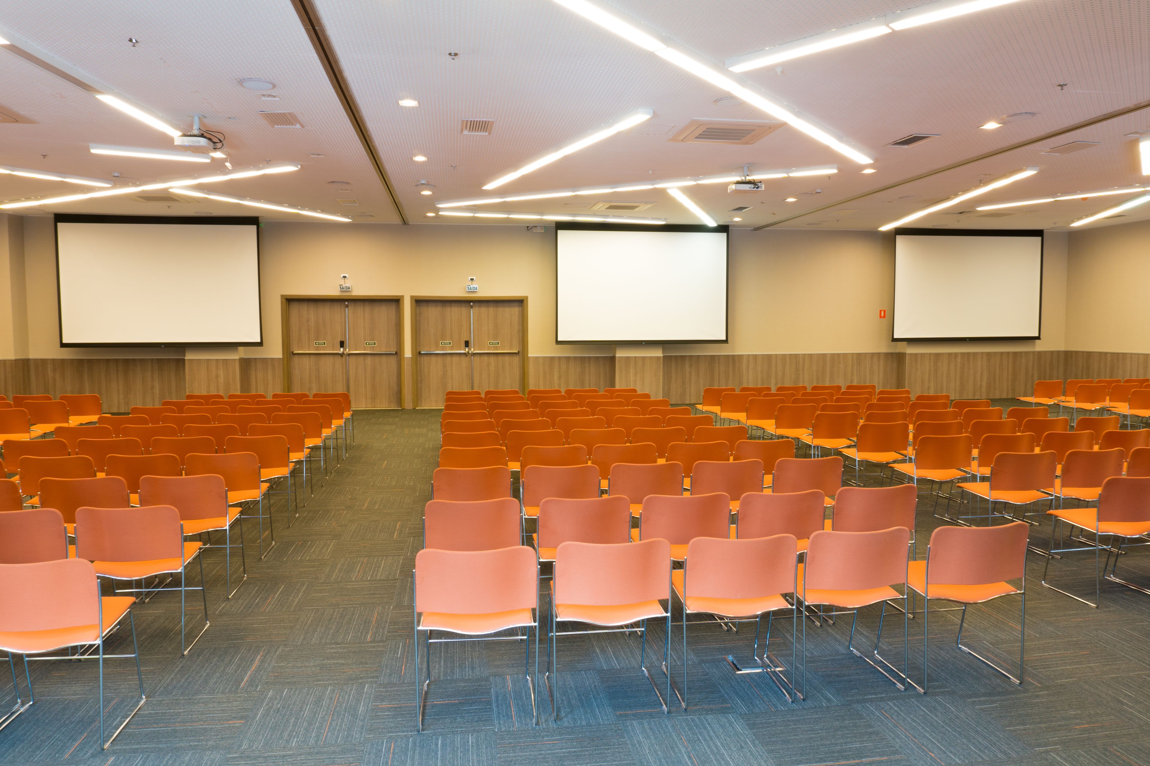 A conference room with rows of orange chairs, a large screen, and a projector.