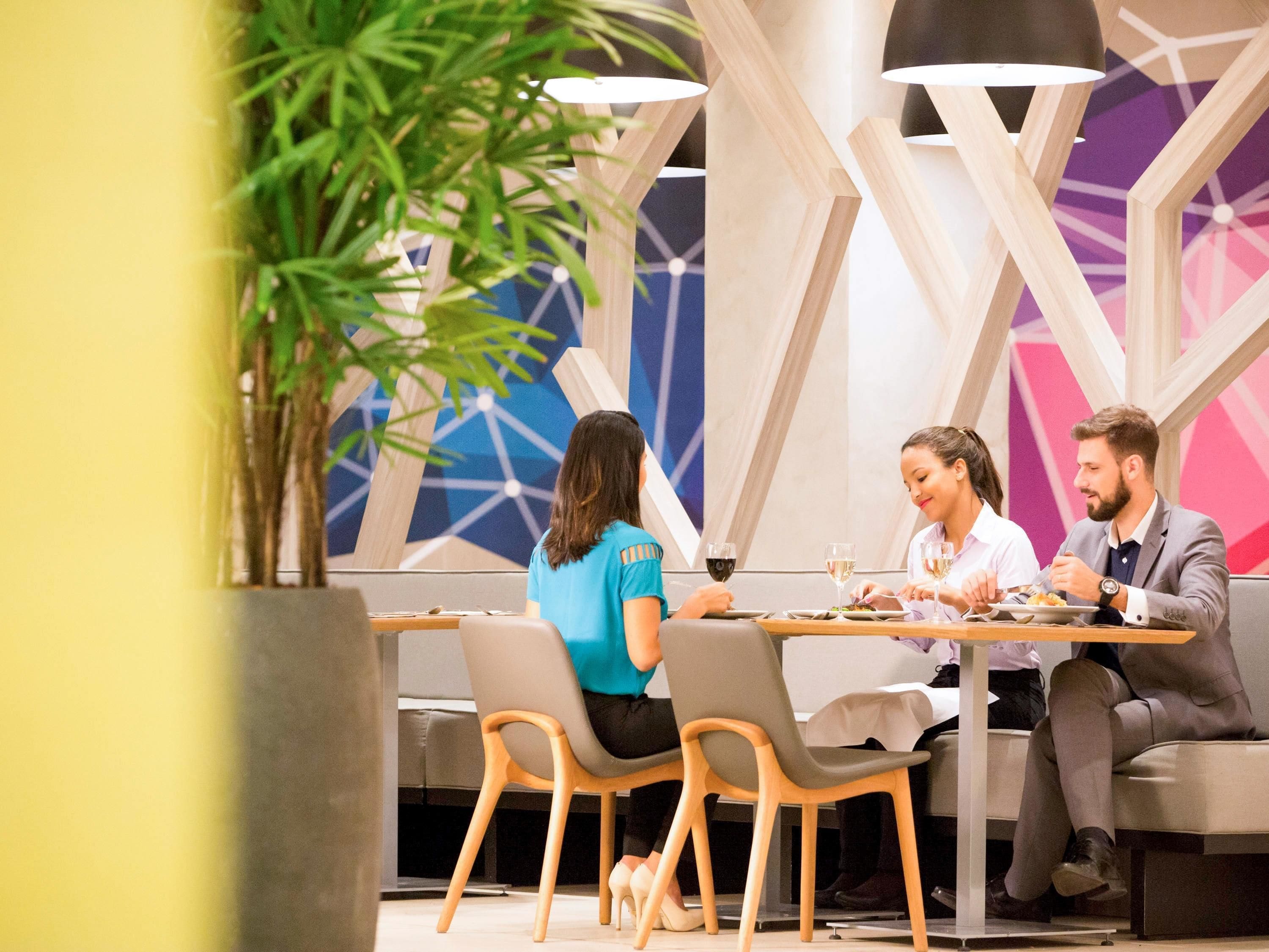 Un comedor moderno con un diseño geométrico en la pared, una planta en maceta y una mesa dispuesta para tres personas.