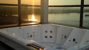 A hot tub with a control panel, set against a backdrop of a large window overlooking a body of water during sunset. - Novotel RJ Porto Atlântico (Rio de Janeiro)