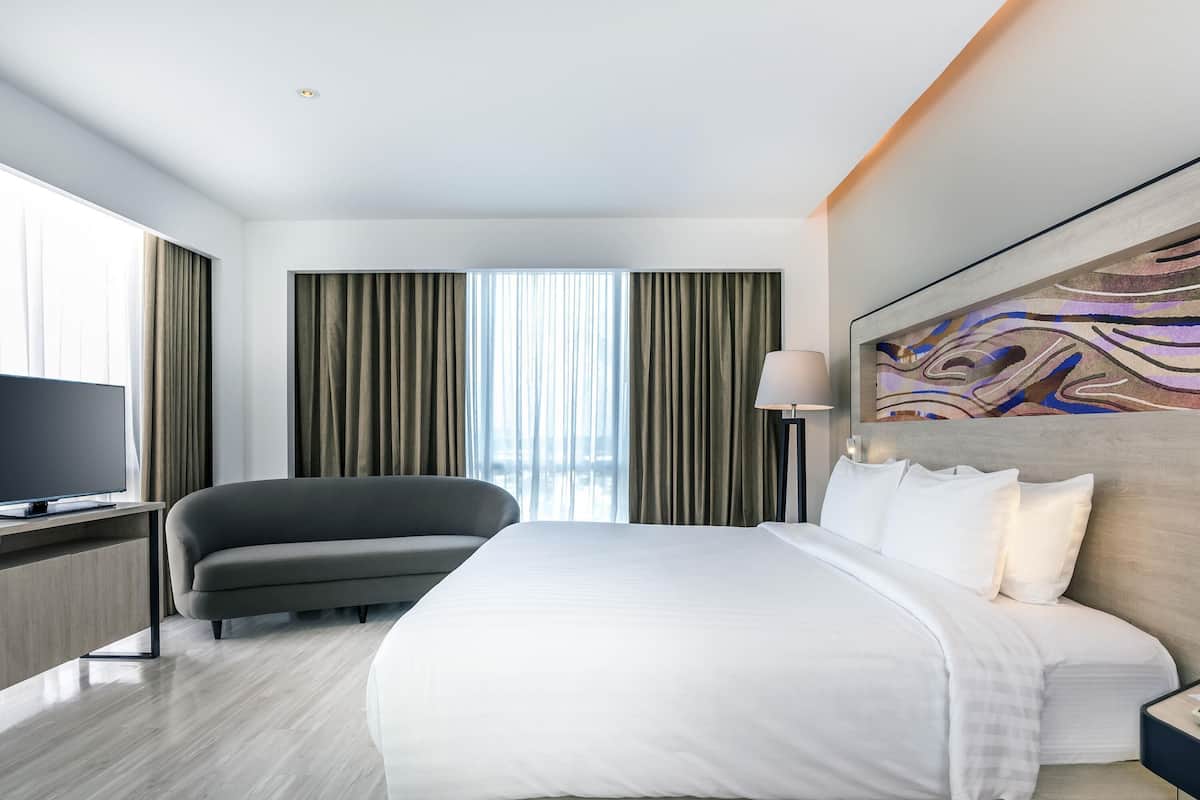 Quarto de hotel moderno com uma cama grande, televisão de tela plana, escrivaninha e uma cadeira.