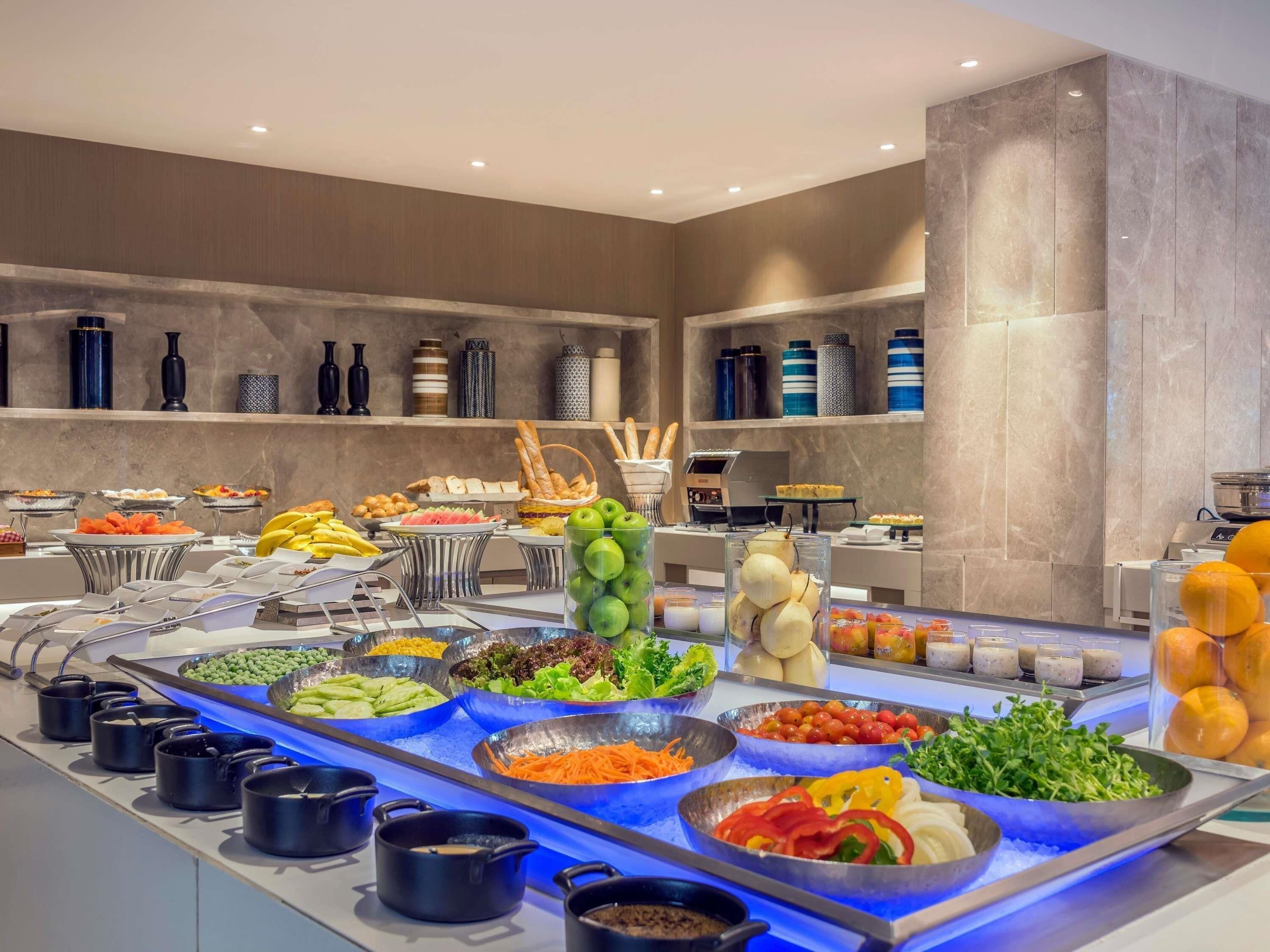 A buffet with various food items and beverages, a kitchen area, and a modern interior design.