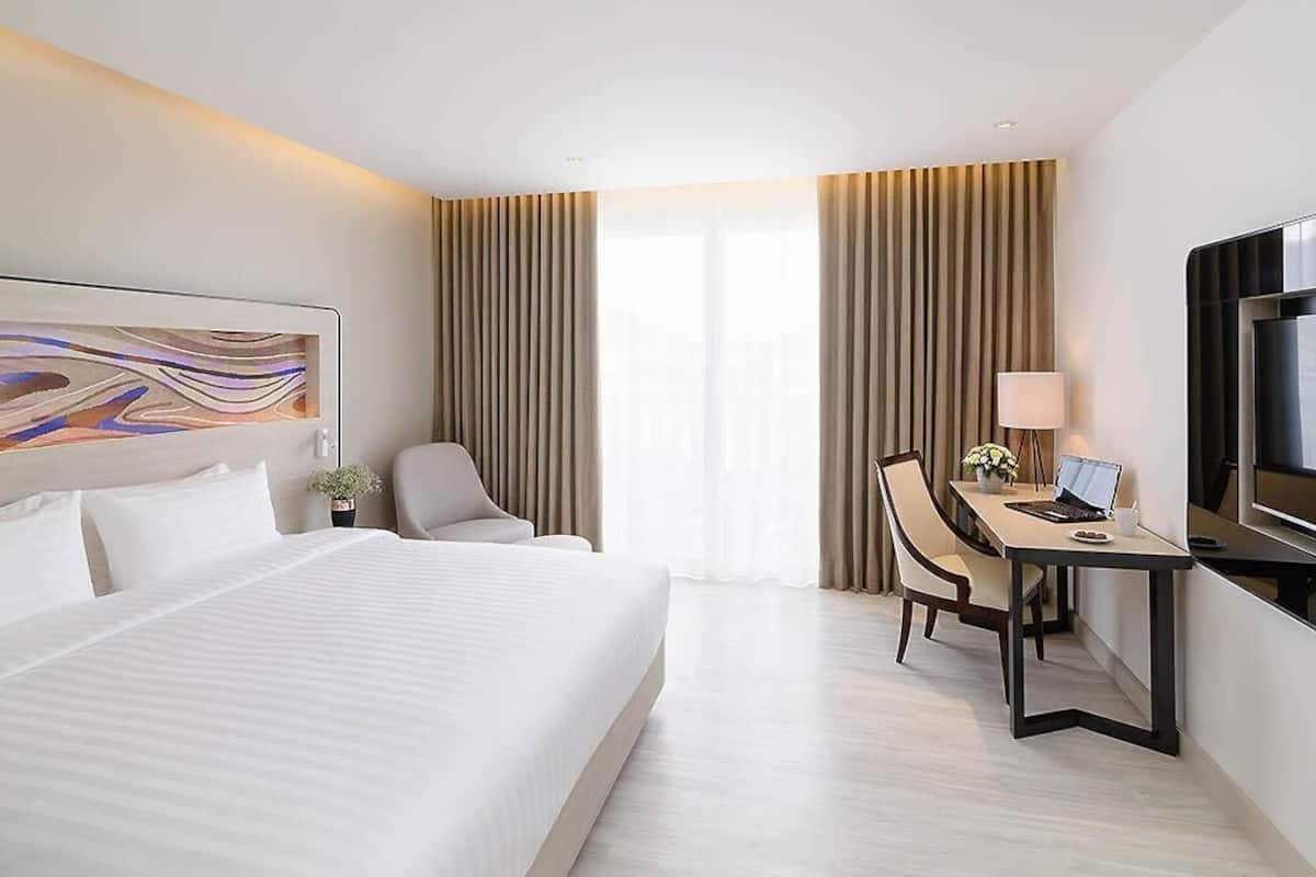 Quarto de hotel com uma cama grande, uma escrivaninha com um laptop, uma televisão e um quadro na parede.