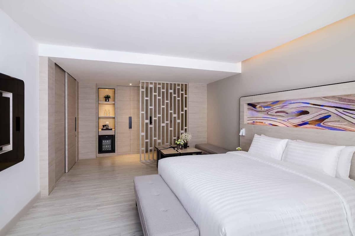 Quarto de hotel moderno com uma cama grande, uma televisão na parede, minibar e um painel decorativo na parede.