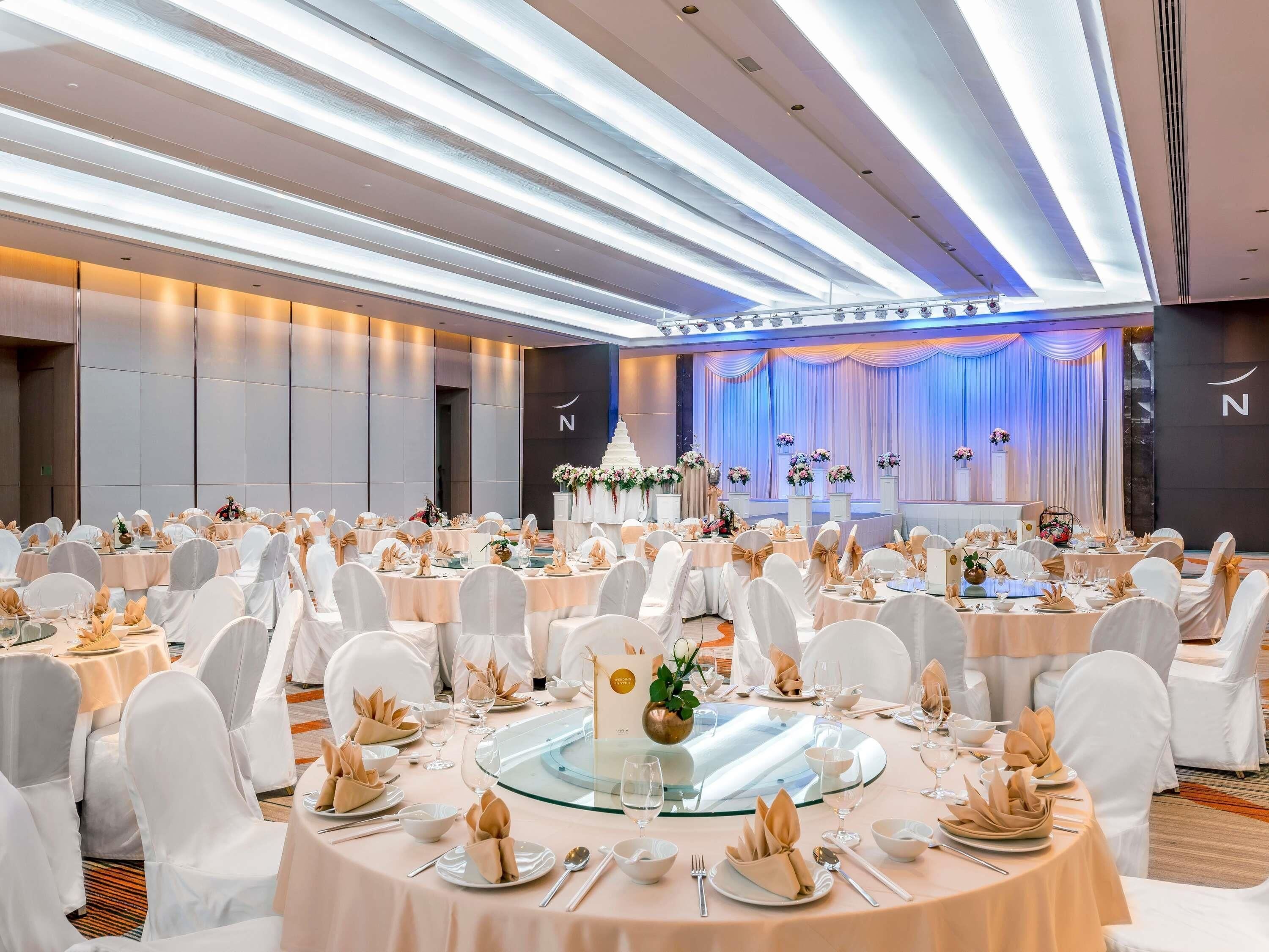 A banquet hall with round tables, white chairs, and a stage with floral decorations.