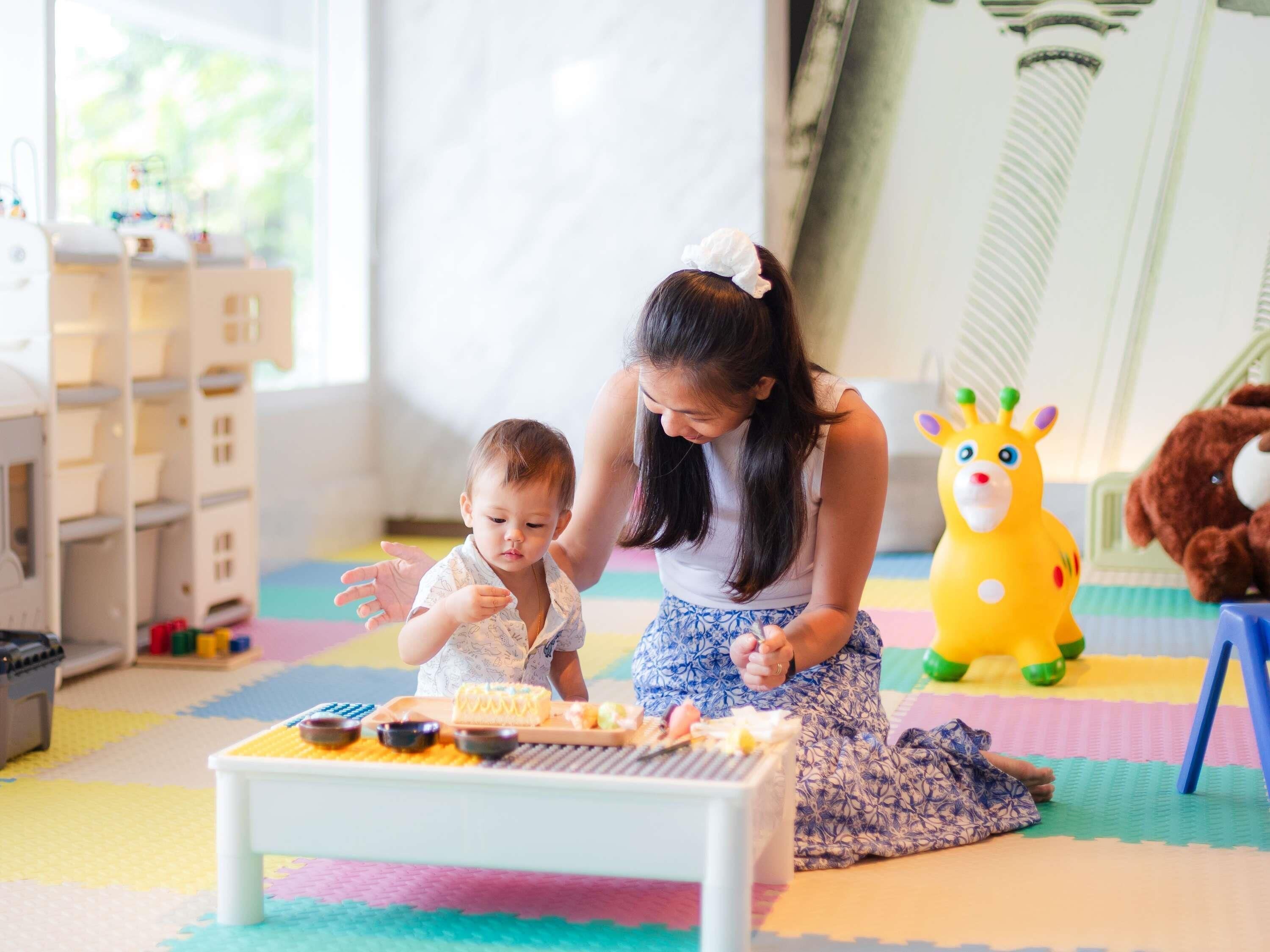 Un niño y un adulto en un cuarto de juegos con una mesa de juegos, juguetes y alfombras de colores.