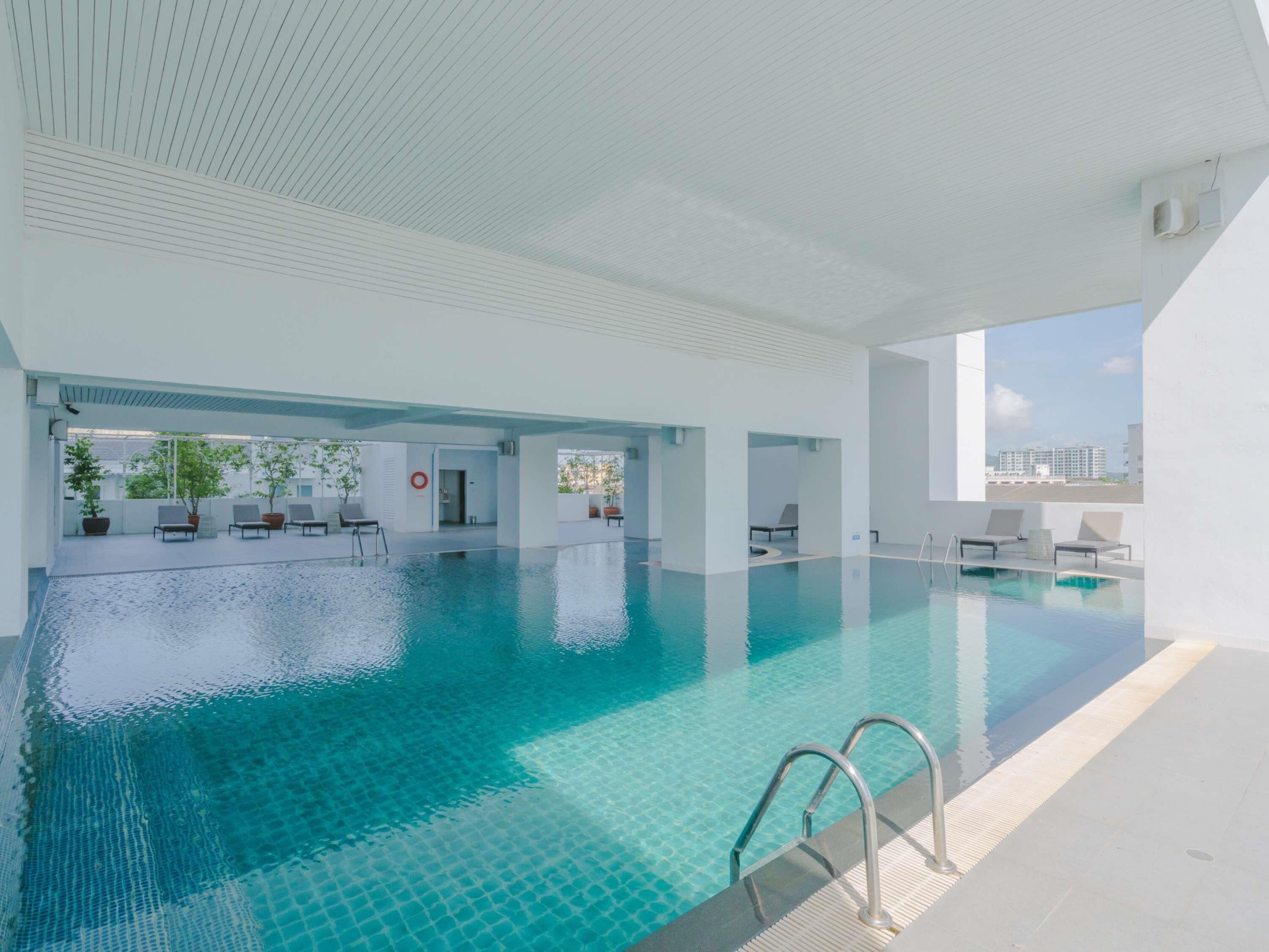 Una piscina interior moderna con agua cristalina, sillas de descanso y vistas a la ciudad.