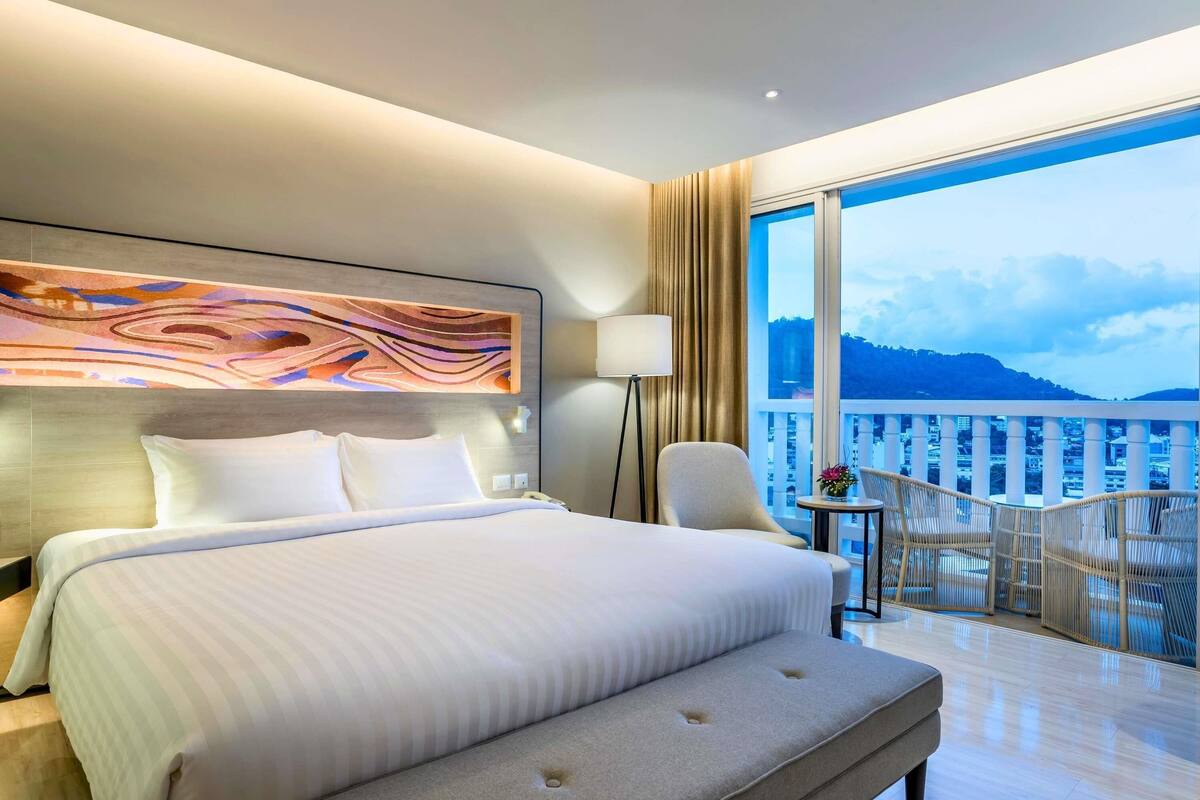 Quarto de hotel com uma cama grande, um sofá, uma cadeira, uma mesa e uma varanda com vista.