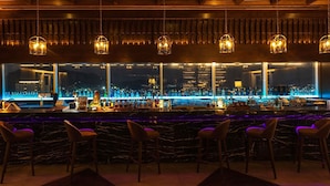 Un bar con vista a la ciudad, techo de madera y lámparas colgantes.