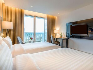 Une chambre d’hôtel avec deux lits, un bureau, une chaise, une télévision et un balcon avec vue.