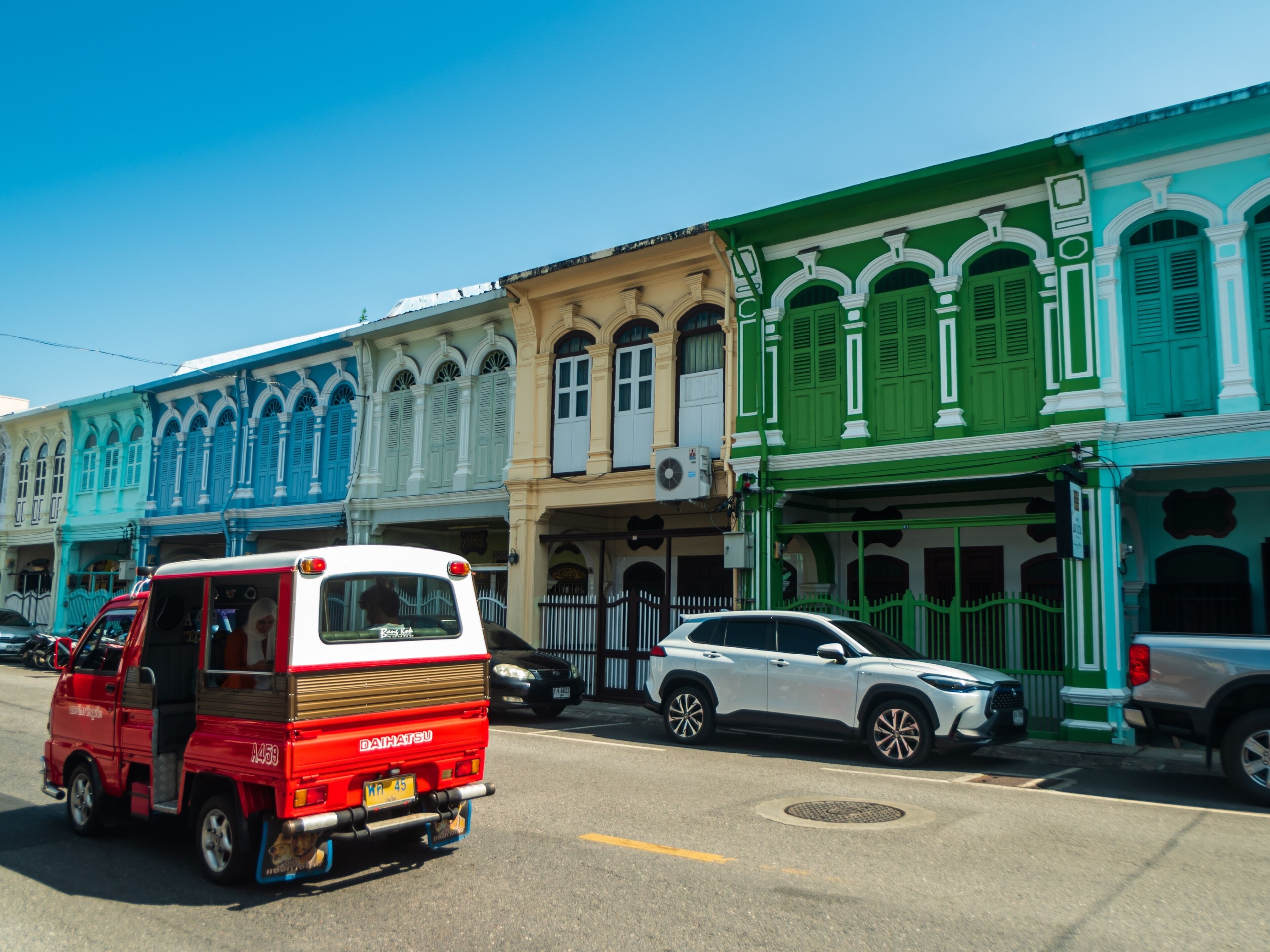 A street with colorful buildings, a red van, and parked cars.