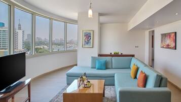 A modern living room with a large window, a flat-screen TV, a blue sofa, and a coffee table.