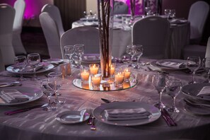 A formal dining table set with plates, glasses, and cutlery, surrounded by candles.
