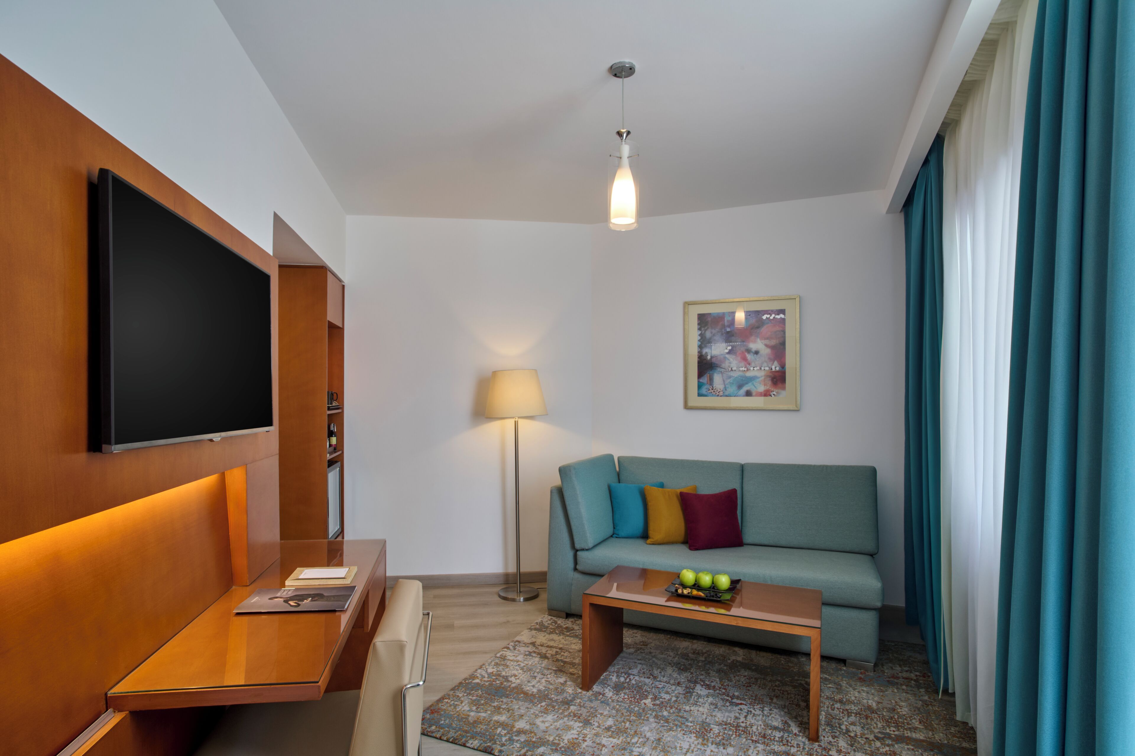 A modern hotel room with a flat-screen TV, a sofa, a coffee table, and a floor lamp.