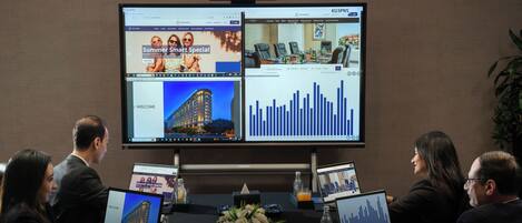 A conference room with a large screen displaying multiple web pages, laptops, and a floral centerpiece.