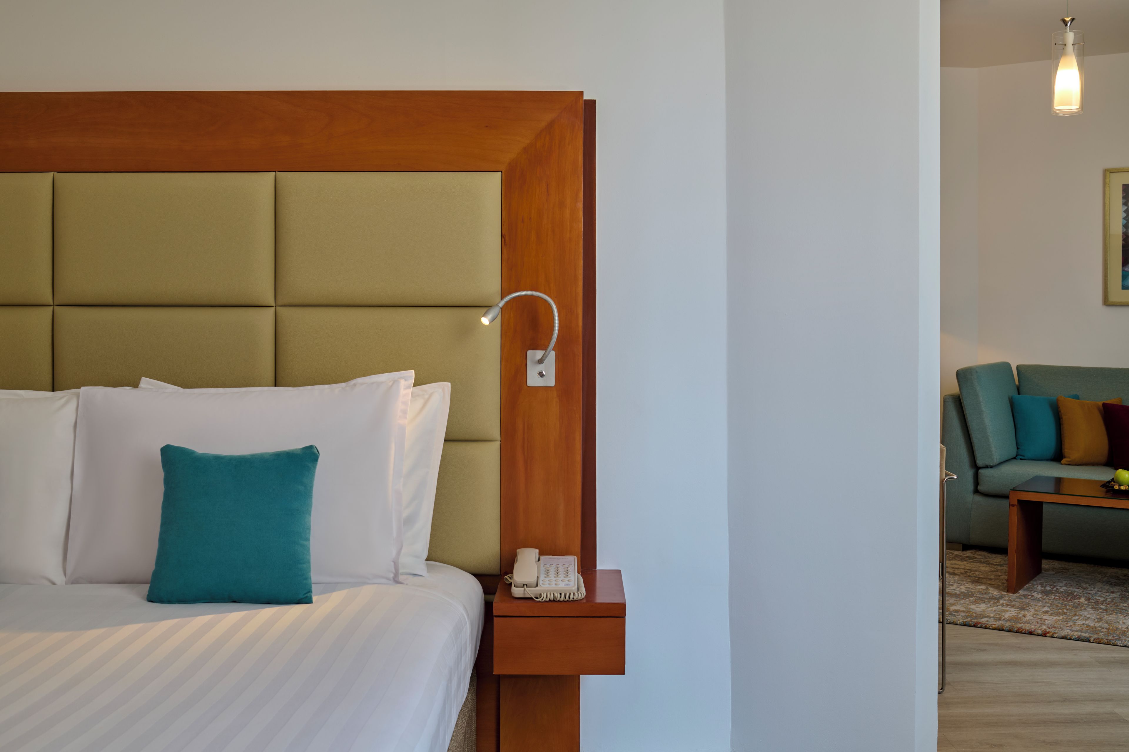 A hotel room with a bed, a bedside table with a phone, and a wall-mounted light fixture.
