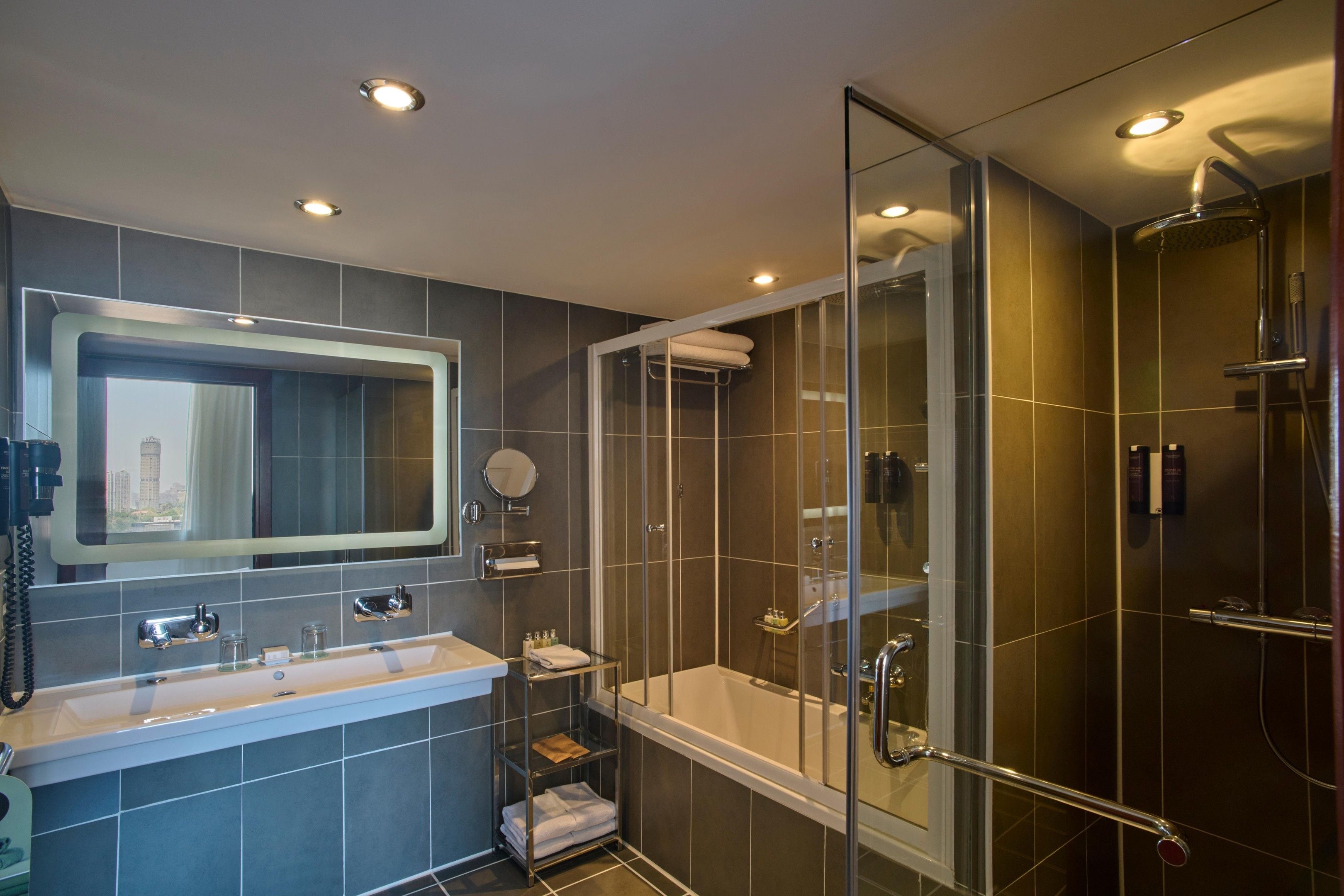 Un baño moderno con bañera, ducha con mampara de vidrio y un espejo grande sobre el lavamanos.