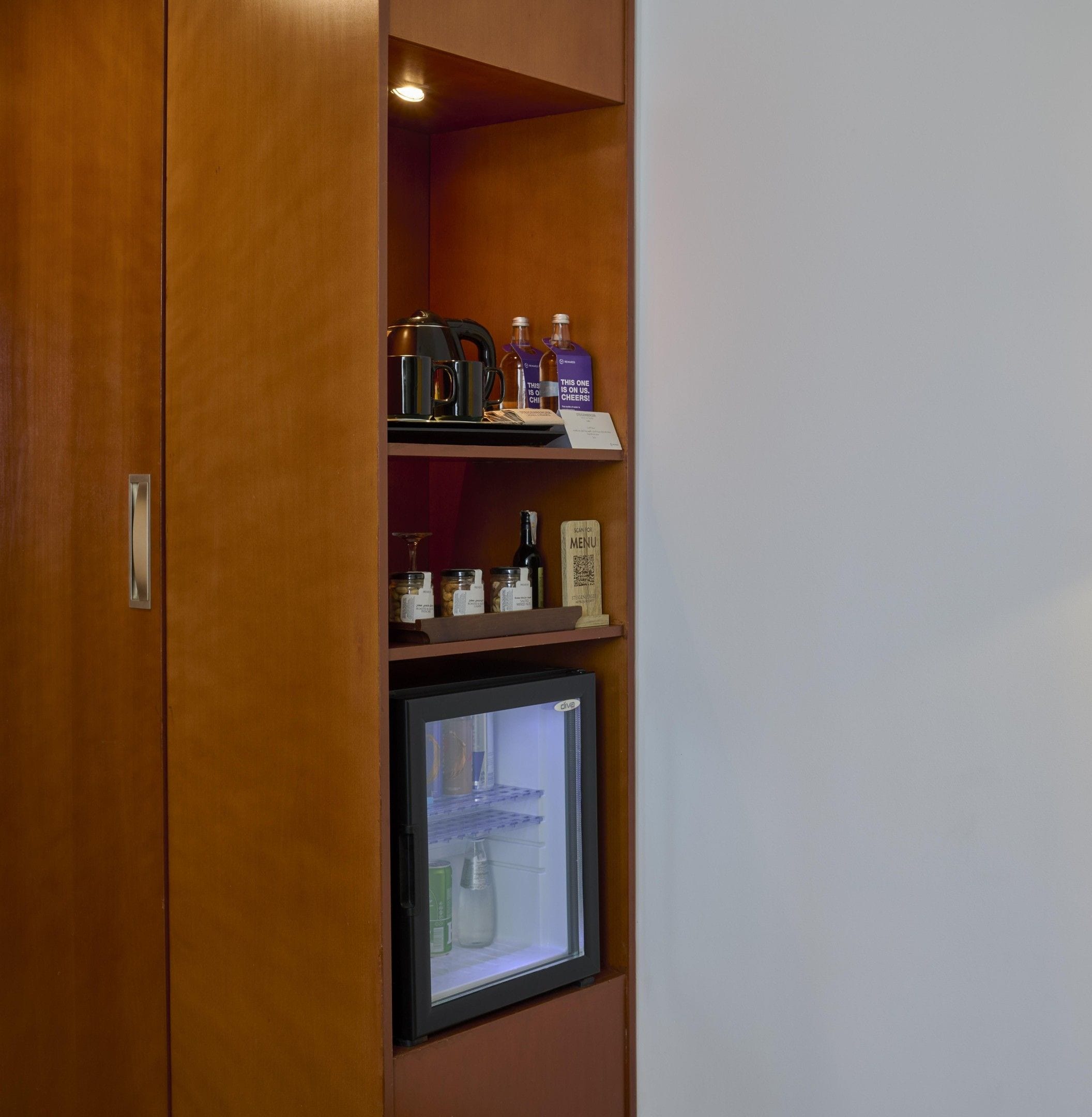 A minibar with a refrigerator, a coffee maker, a bottle of water, and a bottle of wine.
