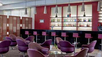 Zona de bar moderna con sillas moradas, pared roja y estanterías llenas de botellas de licor.