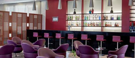 A modern bar area with purple chairs, a red wall, and shelves of liquor bottles.