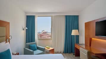 Quarto de hotel com cama, escrivaninha, cadeira, televisão e janela com cortinas.