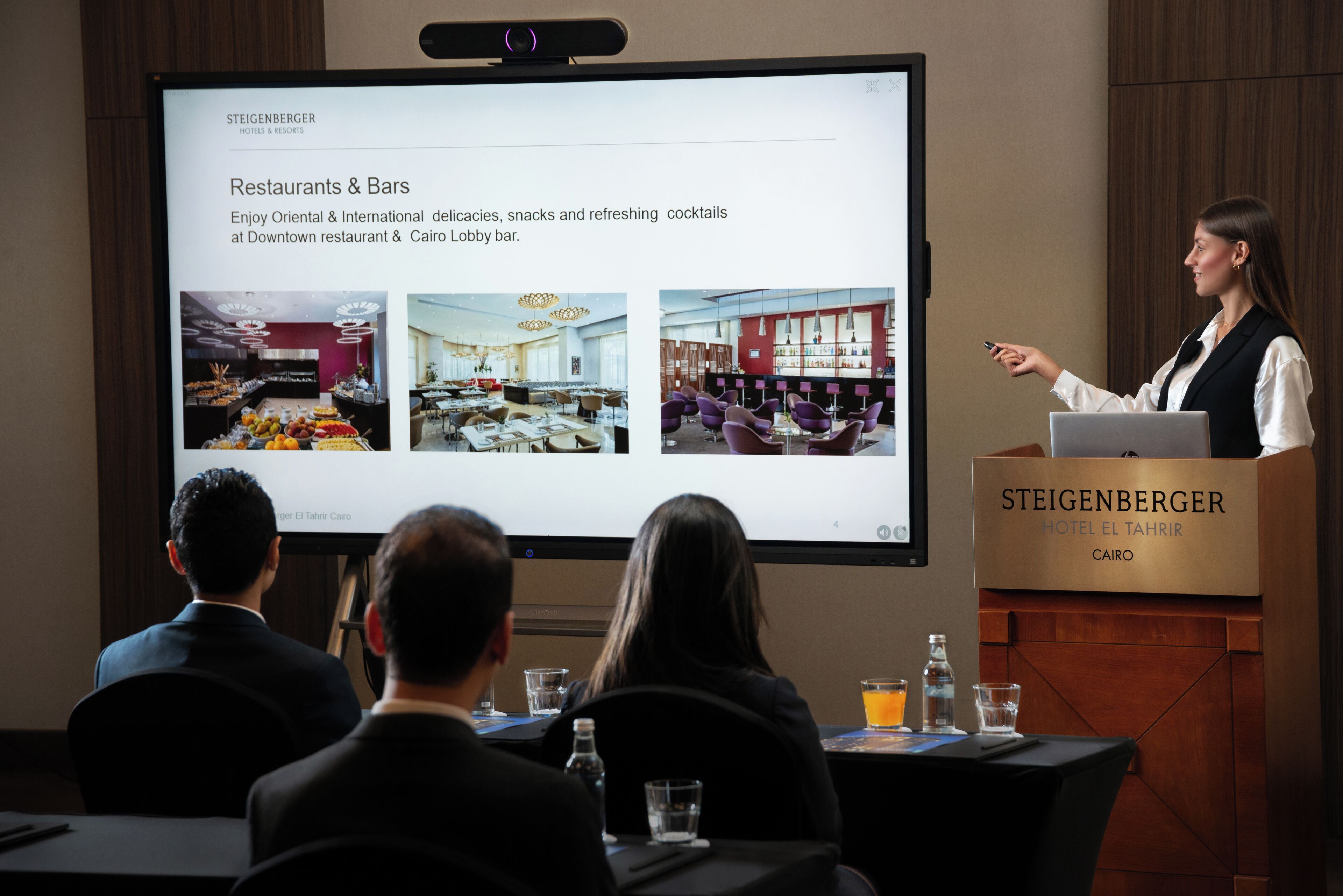 A presentation in a hotel conference room with a screen displaying restaurant and bar options.