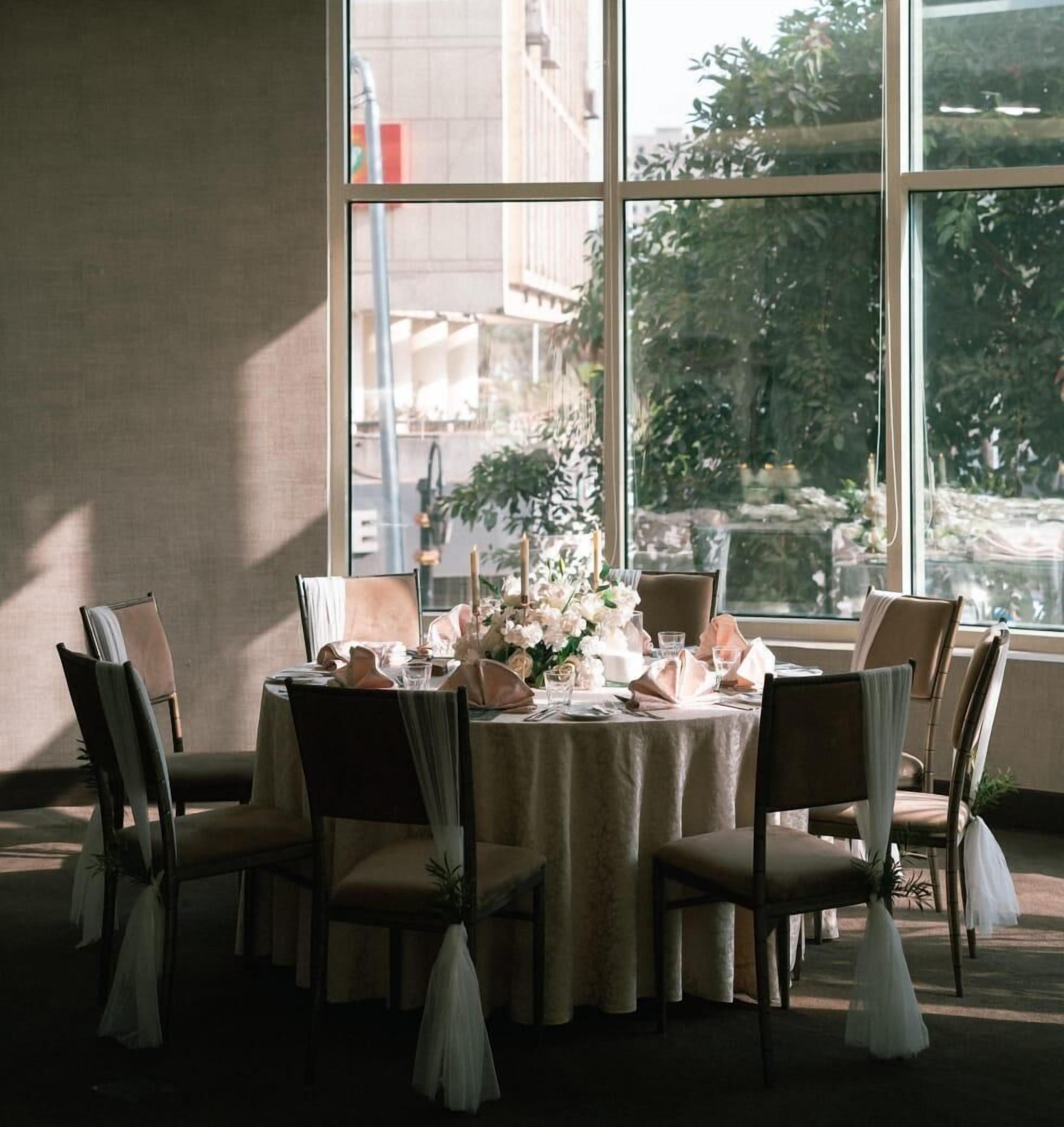 Ein runder Tisch mit Stühlen, eine Vase mit Blumen und Blick durch große Fenster.