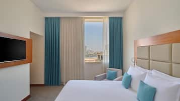 A hotel room with a bed, a television, a view of the city, and a window with curtains.