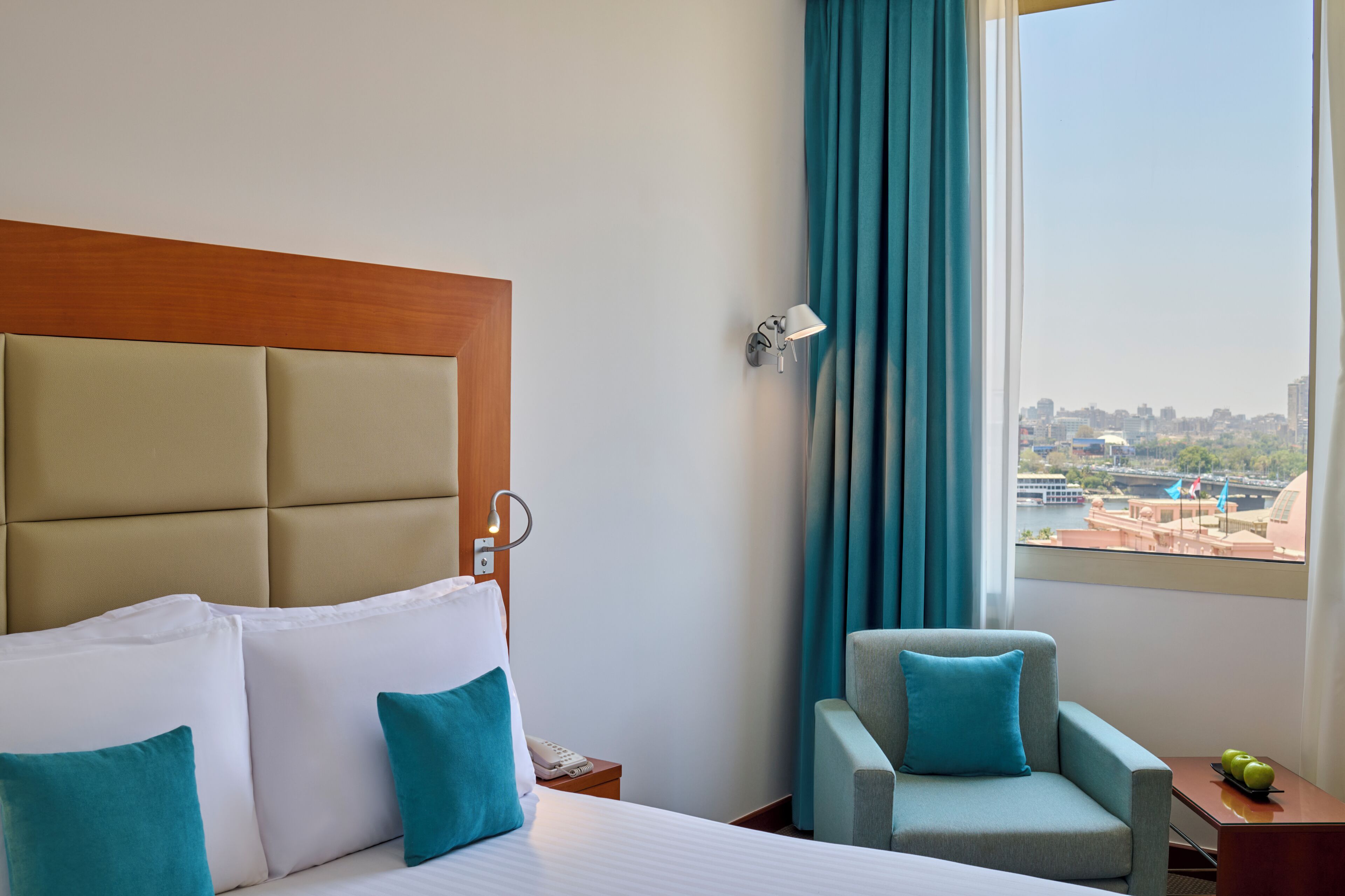Camera d'albergo con un letto grande, una poltrona, un comodino e vista sulla città attraverso la finestra.