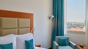 Camera d'albergo con un letto grande, una poltrona, un comodino e vista sulla città attraverso la finestra.