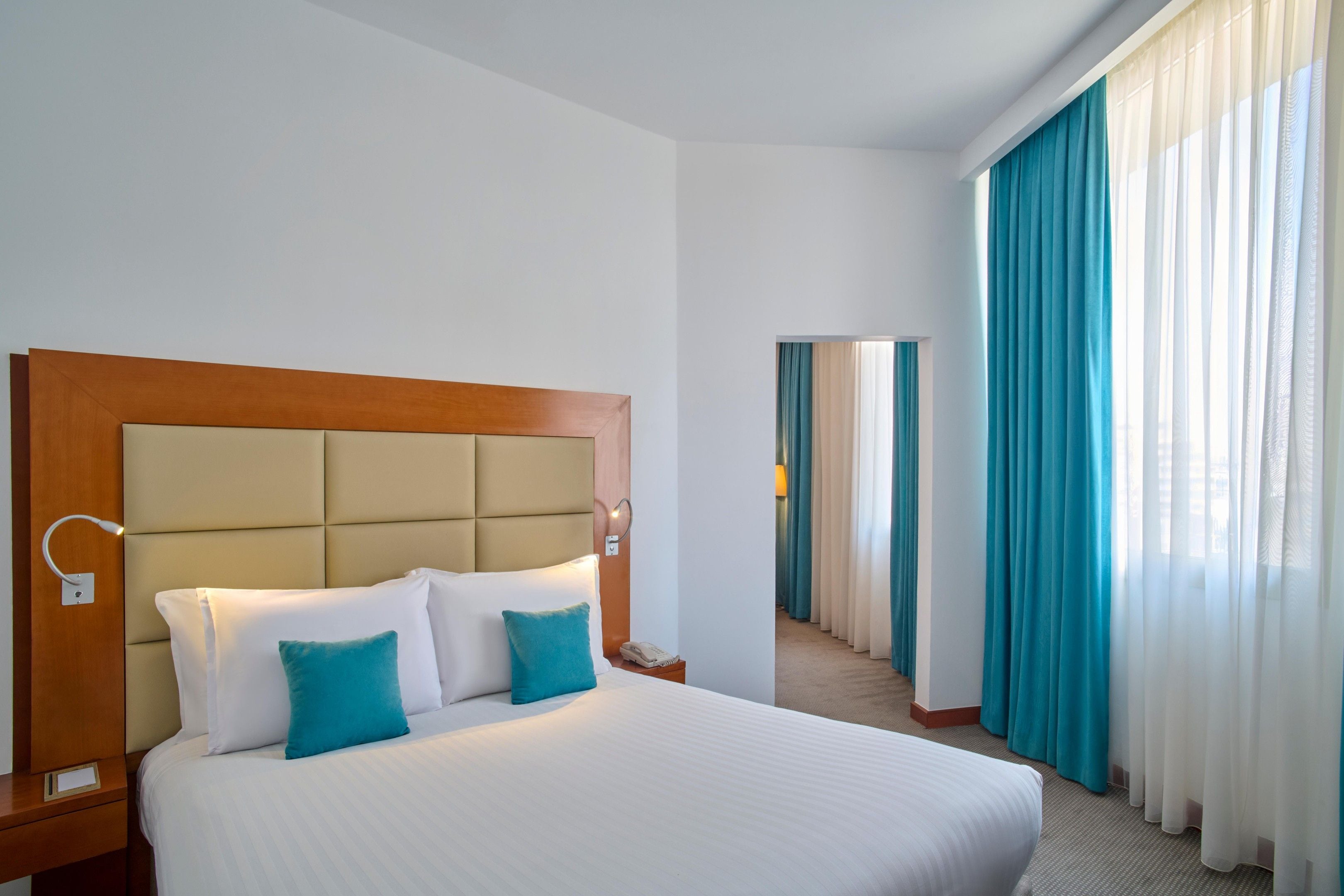 A hotel room with a large bed, a headboard, a bedside table, a lamp, and a telephone.