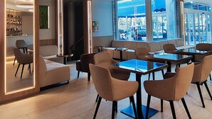Un moderno vestíbulo de hotel con zona de estar, un bar y grandes ventanales que ofrecen vistas de la ciudad.