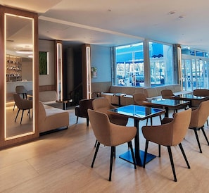 En moderne hotellobby med siddeområde, bar og store vinduer med udsigt over byen.