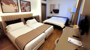 Habitación de hotel con dos camas, un escritorio, una silla, un televisor y una obra de arte en la pared.