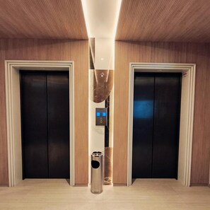 A hallway with two elevators, a trash bin, and a modern light fixture. - Hotel Vittoria Parc (Bari)