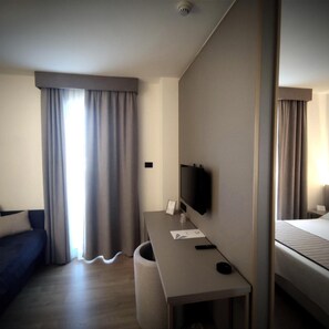 A hotel room with a bed, a desk with a television, a chair, and a window with curtains. - Vittoria Parc Hotel (Bari)