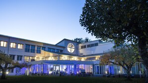 Un bâtiment moderne doté d’une grande fenêtre circulaire, d’un espace extérieur aménagé pour s’asseoir et d’une partie couverte éclairée de lumière bleue.