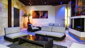 Un hall d’entrée moderne avec un espace salon comprenant des canapés et une table basse, une grande plante et des œuvres d’art murales abstraites.