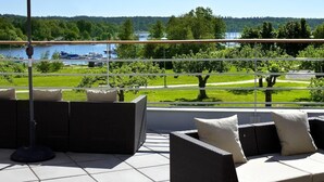 Une terrasse extérieure aménagée avec des meubles en osier et de grands parasols, offrant une vue sur un lac et la verdure environnante.