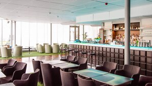 Un espace bar moderne doté d’un long comptoir, de tabourets et d’un coin salon avec des tables et des chaises.