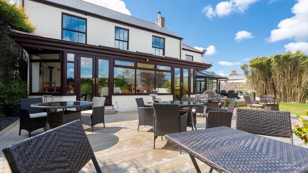 Une vaste terrasse extérieure aménagée avec des meubles en osier et un coin repas fermé par des parois de verre.