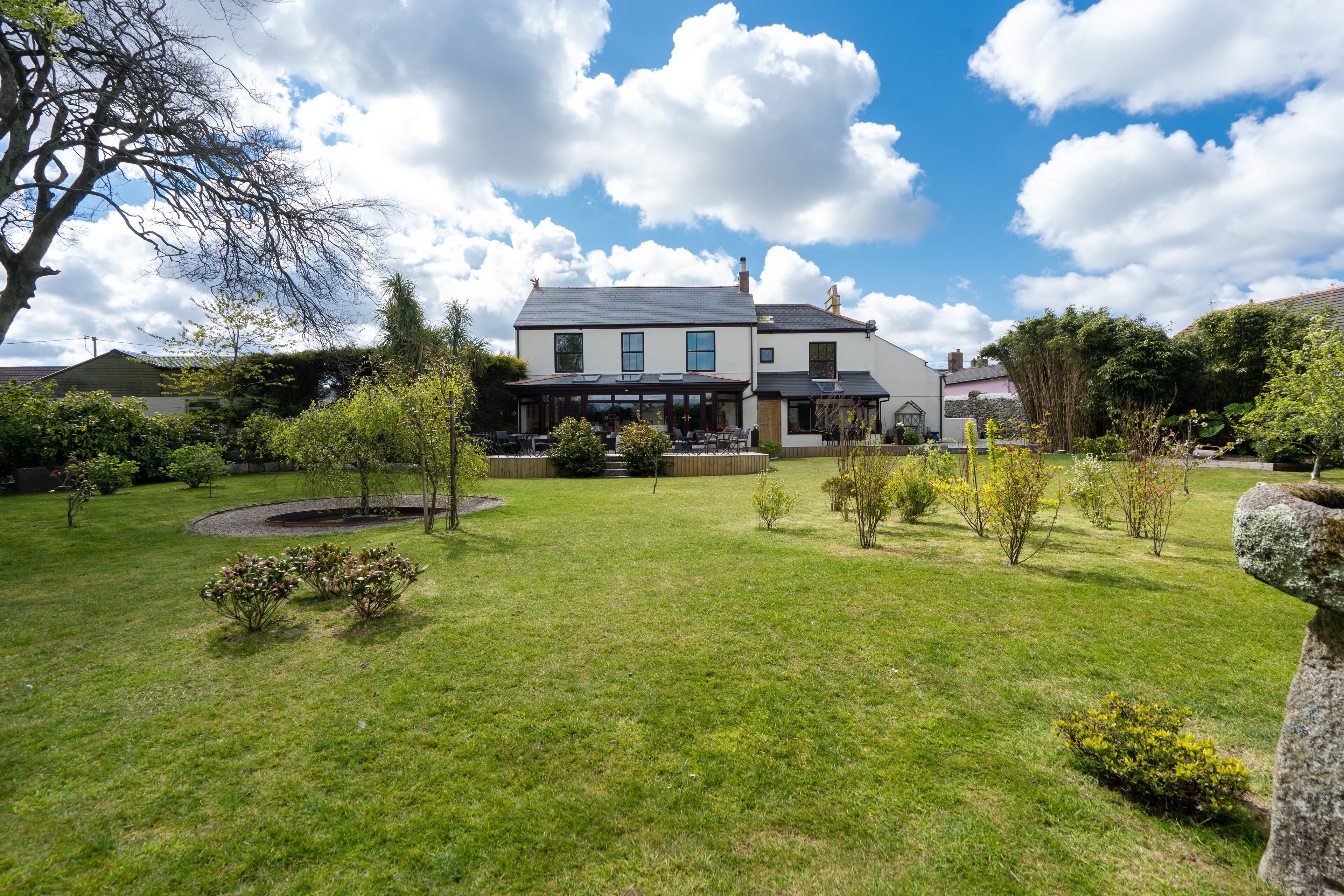 A large house with a well-maintained lawn, a stone sculpture, and a variety of shrubs and trees.