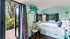 Une chambre à coucher avec un lit, une chaise, une fenêtre avec des rideaux, une étagère avec des vêtements et une vue sur l’extérieur.