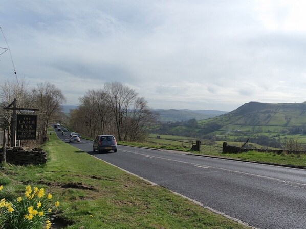 A road with a sign for The Lamb Inn, a bar, and food. - The Lamb Inn (High Peak)