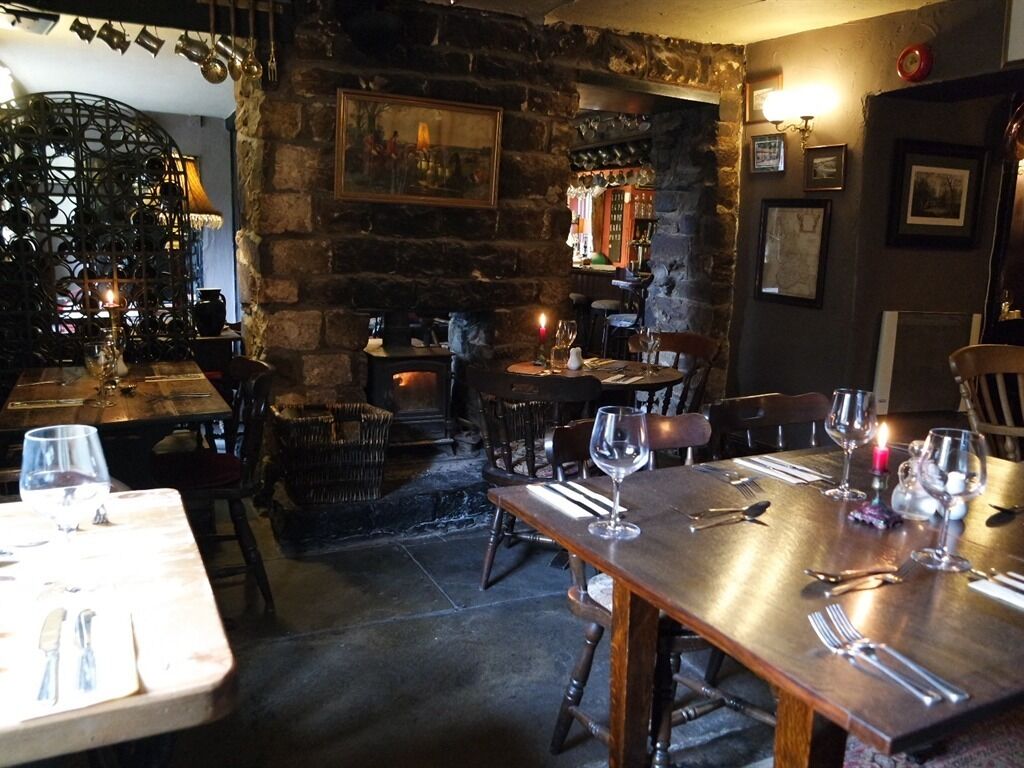 Interior rústico de restaurante, com paredes de pedra, mesas e cadeiras de madeira.