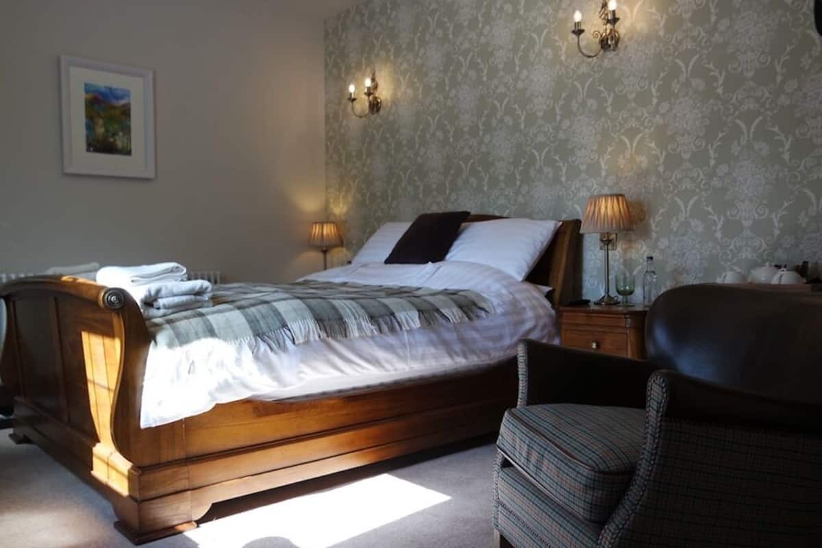 Ein Schlafzimmer mit einem hölzernen Bett, zwei Nachttischlampen, einem Sessel und einem an der Wand hängenden Bild.