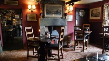Un coin repas chaleureux avec des tables et des chaises en bois, une cheminée et des lampes fixées au mur.