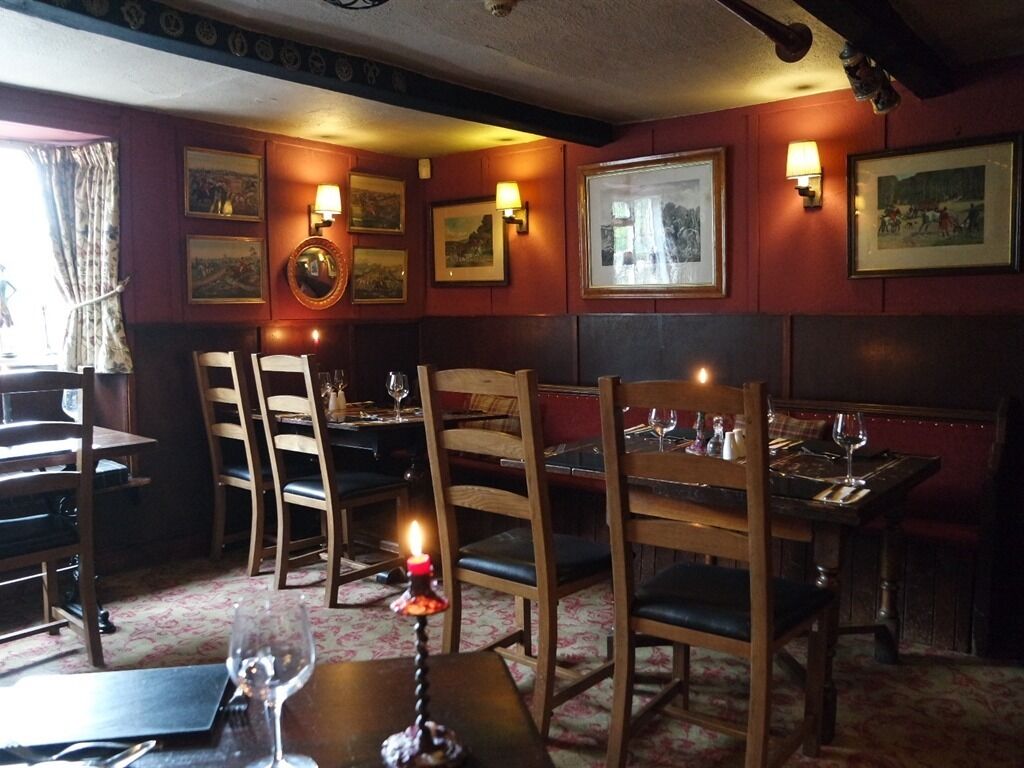 A restaurant interior with wooden tables and chairs, framed pictures on the walls, and a candle on one table.