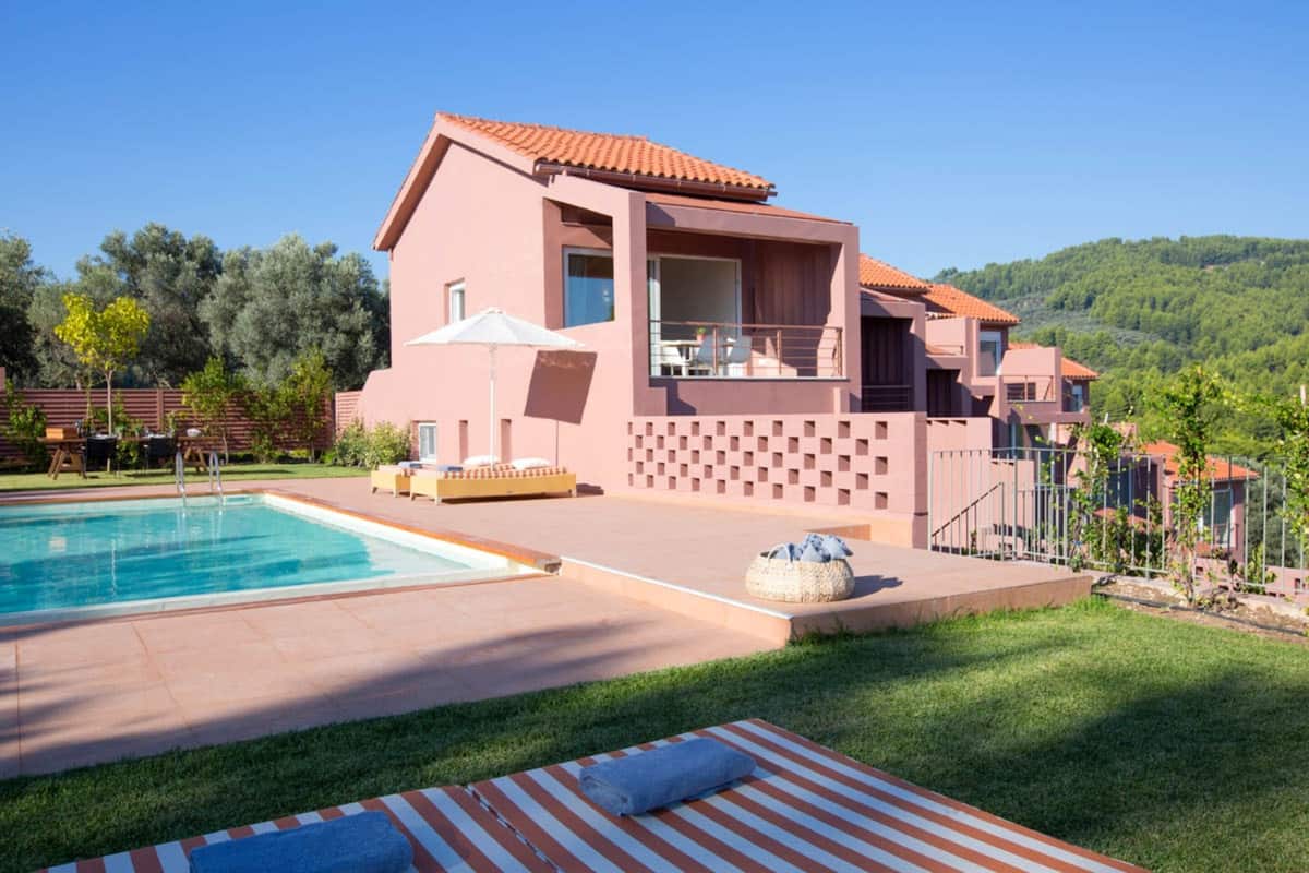 A modern two-story house with a swimming pool, outdoor seating, and a view of the surrounding hills.